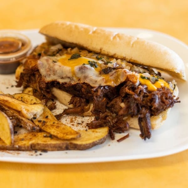 Arod's Tex Mex sandwich with shredded meat, melted cheese, and a side of potato wedges.