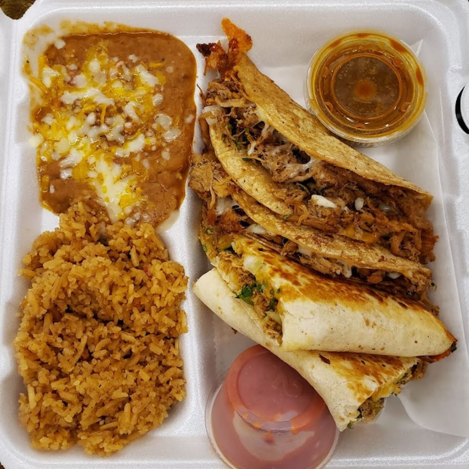 Arod's Tex Mex birria tacos, refried beans with cheese, Mexican rice, and dipping sauces in a takeout container.