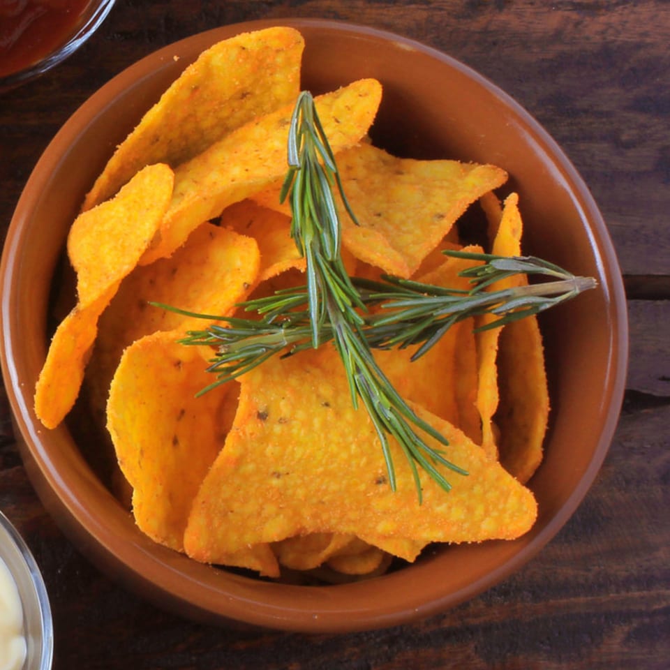 Arod's Tex Mex tortilla chips in a brown bowl, garnished with rosemary, on a wooden table.